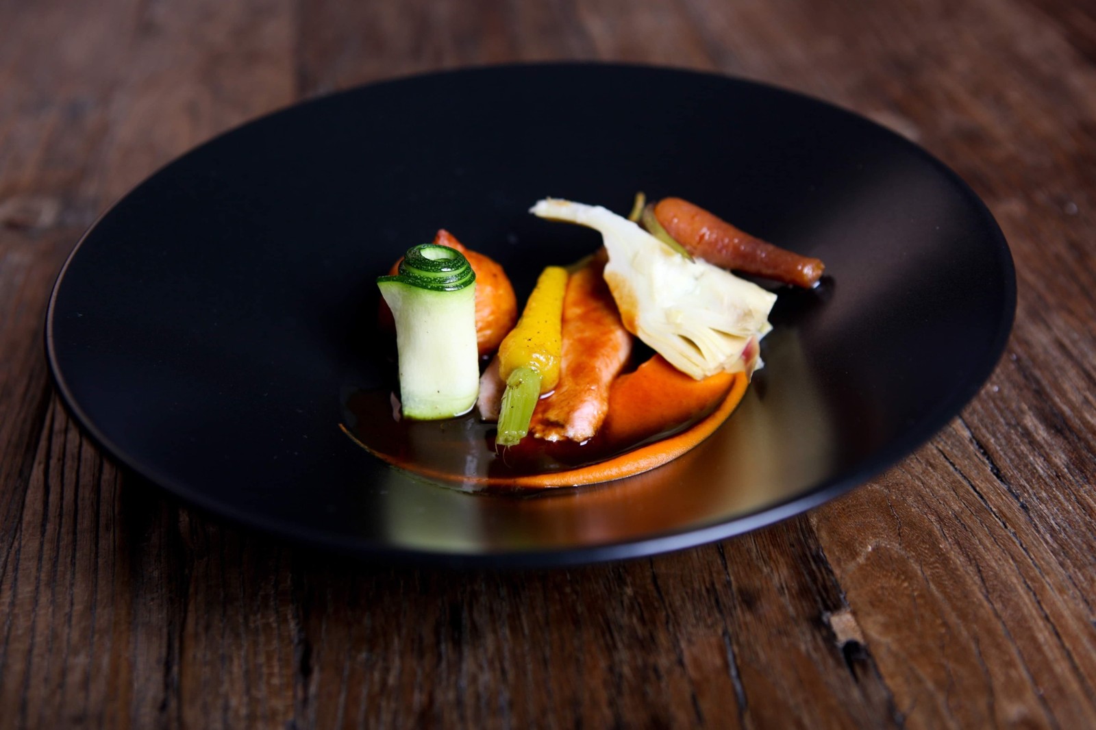 Een verfijnd gerecht met kleurrijke groenten op een zwart bord