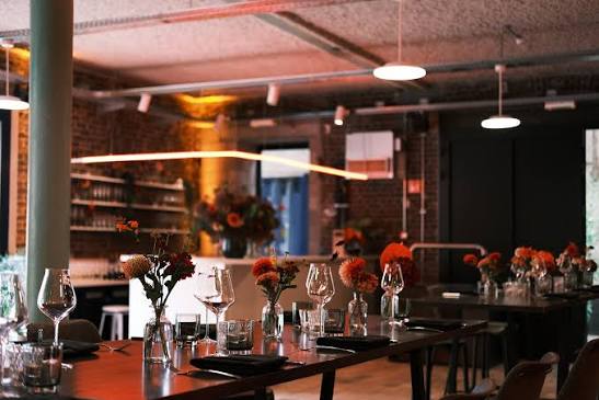 Gedekte tafels met bloemen in het warme industriële interieur van Zaal Bartsoen